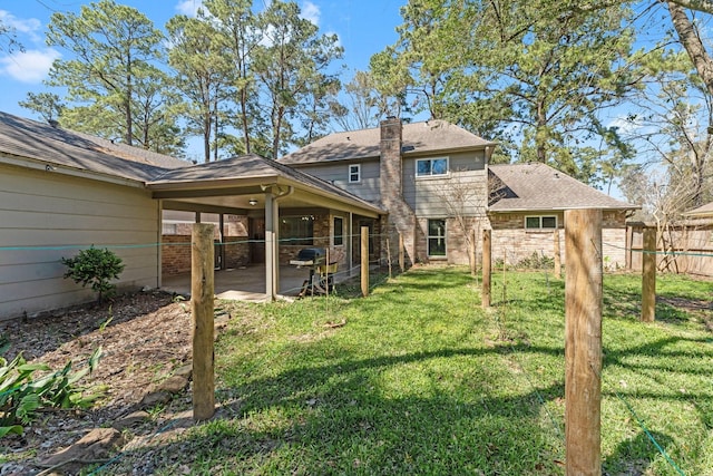 rear view of property with fence, a yard, brick siding, a chimney, and a patio area