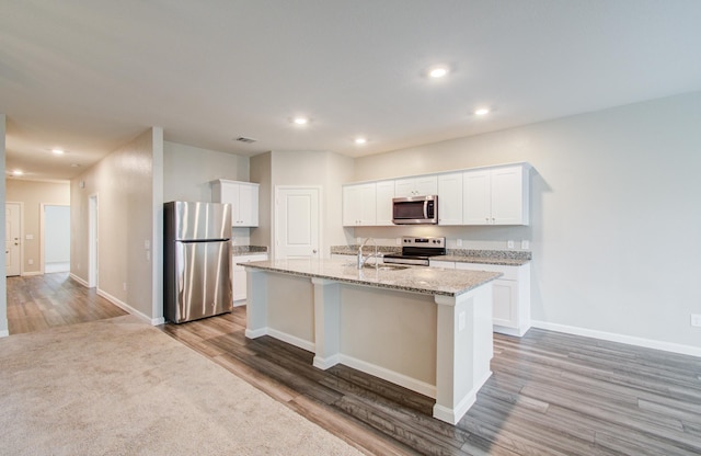 kitchen with a center island with sink, light wood-type flooring, appliances with stainless steel finishes, white cabinetry, and a sink