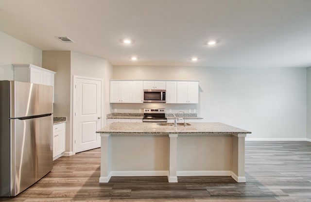 kitchen featuring light stone countertops, visible vents, an island with sink, a sink, and stainless steel appliances