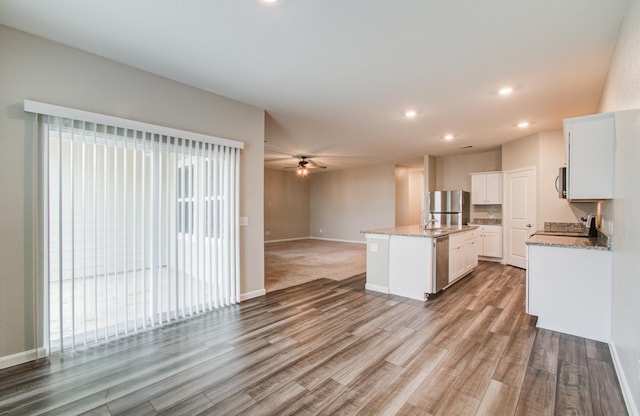 kitchen featuring an island with sink, open floor plan, stainless steel appliances, light wood-style floors, and ceiling fan