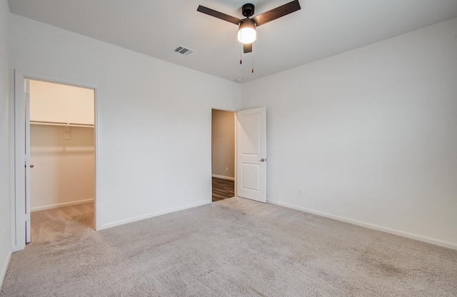 unfurnished bedroom with visible vents, a walk in closet, ceiling fan, baseboards, and carpet