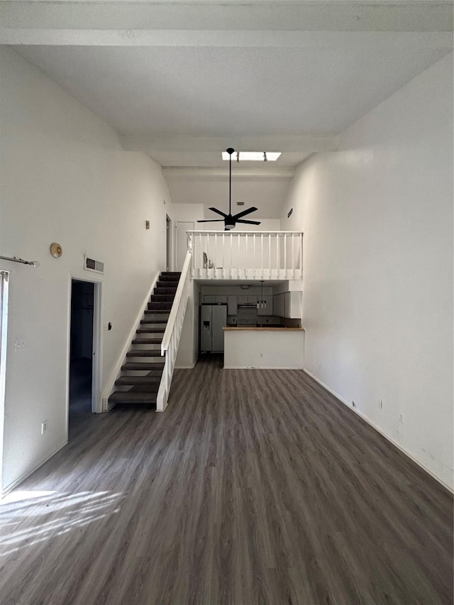 unfurnished living room with visible vents, lofted ceiling with beams, dark wood-style floors, ceiling fan, and stairs