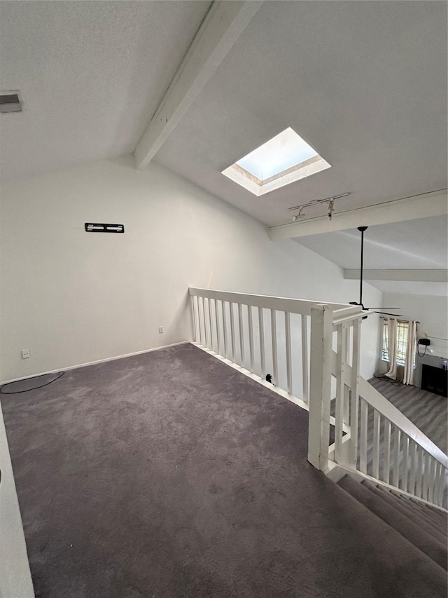 carpeted empty room with lofted ceiling with skylight, rail lighting, and baseboards