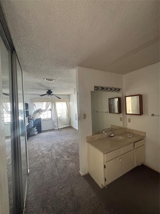 interior space with a textured ceiling, visible vents, dark carpet, and a sink