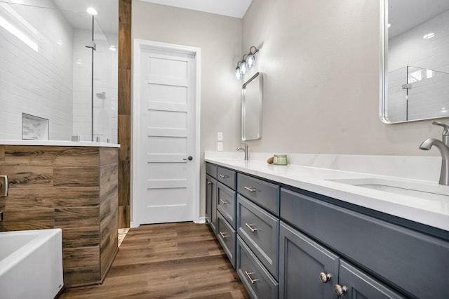 full bath with a tile shower, double vanity, wood finished floors, and a sink