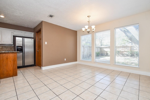 kitchen featuring tasteful backsplash, baseboards, a chandelier, pendant lighting, and stainless steel fridge