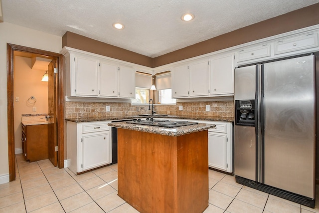 kitchen with light tile patterned flooring, white cabinets, stainless steel fridge, backsplash, and a center island