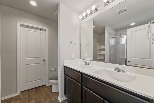 full bathroom with visible vents, toilet, double vanity, wood finished floors, and a sink