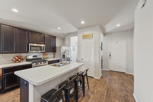 kitchen with light wood-type flooring, a sink, a kitchen breakfast bar, appliances with stainless steel finishes, and light countertops