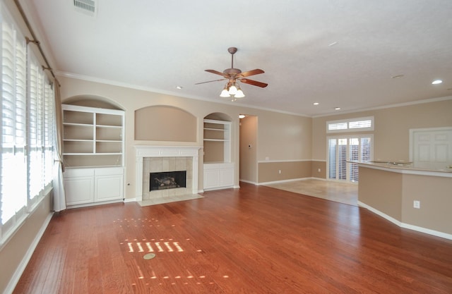 unfurnished living room featuring wood finished floors, built in features, a fireplace, and visible vents