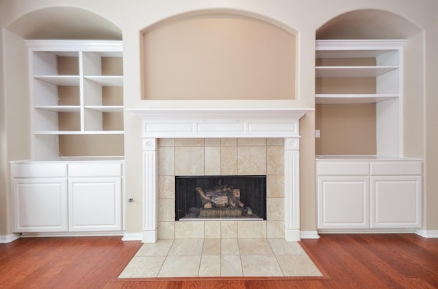 unfurnished living room featuring a tiled fireplace, built in shelves, wood finished floors, and baseboards