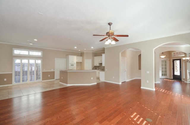 unfurnished living room featuring light wood-style flooring, ceiling fan with notable chandelier, baseboards, and a wealth of natural light