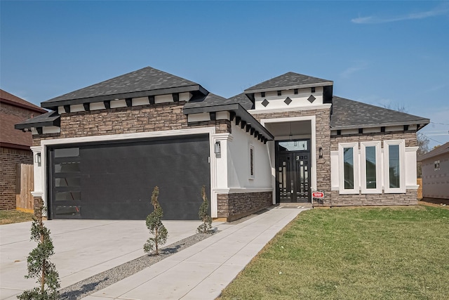 prairie-style house featuring a front lawn, driveway, stone siding, a shingled roof, and a garage