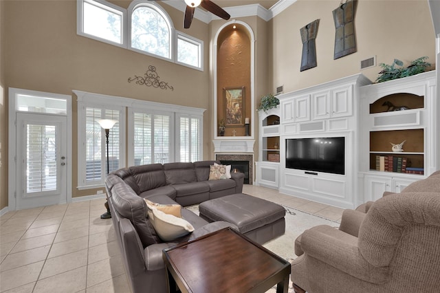 living room with visible vents, built in shelves, a warm lit fireplace, light tile patterned flooring, and a towering ceiling