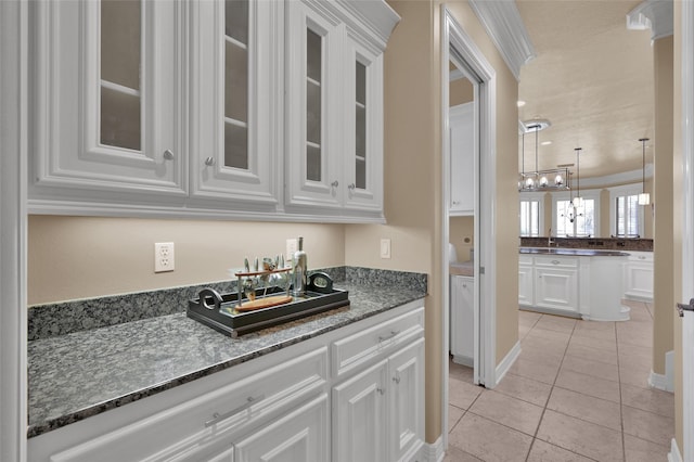 kitchen featuring glass insert cabinets, pendant lighting, dark stone counters, light tile patterned floors, and white cabinets