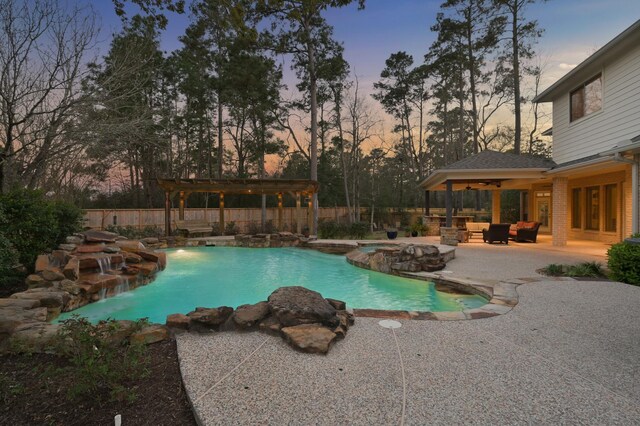 pool at dusk with an in ground hot tub, a patio area, fence, and ceiling fan