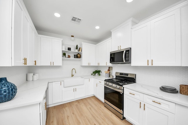 kitchen with light wood finished floors, visible vents, a sink, stainless steel appliances, and open shelves