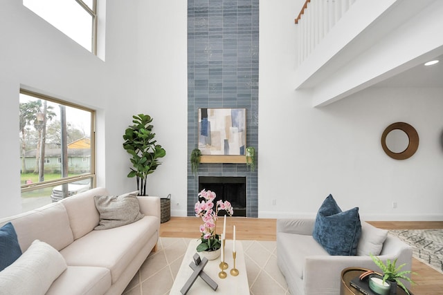 living area with baseboards, a large fireplace, wood finished floors, and a towering ceiling