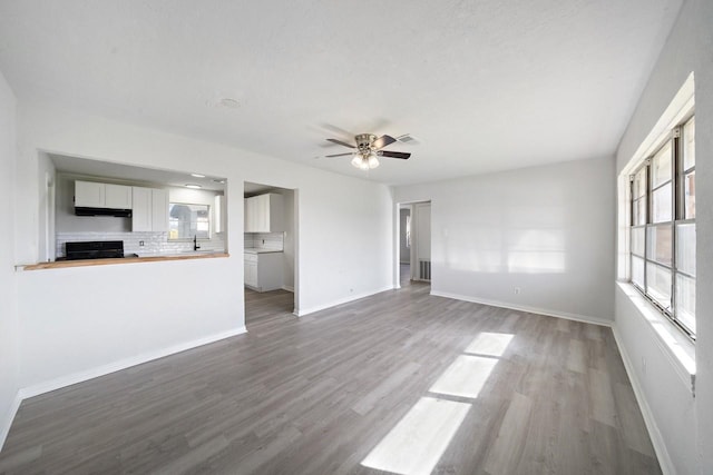 unfurnished living room featuring a healthy amount of sunlight, a ceiling fan, baseboards, and wood finished floors