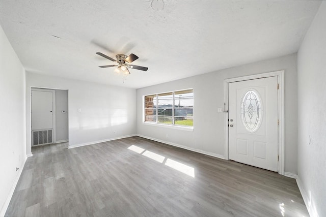 entryway featuring a ceiling fan, visible vents, wood finished floors, baseboards, and a textured ceiling