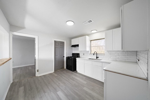 kitchen featuring visible vents, a sink, under cabinet range hood, backsplash, and black gas stove