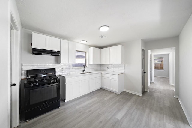 kitchen with a sink, decorative backsplash, under cabinet range hood, black range with gas stovetop, and white cabinetry