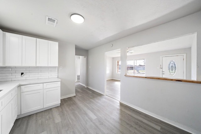 kitchen with tasteful backsplash, visible vents, light wood-type flooring, light countertops, and white cabinetry