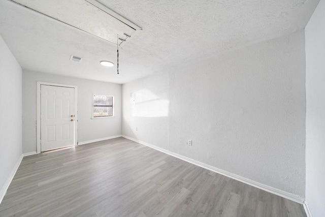 unfurnished room featuring visible vents, baseboards, attic access, wood finished floors, and a textured ceiling