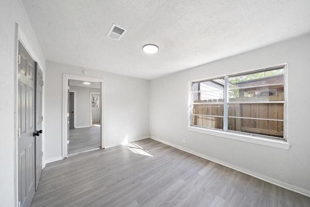 spare room featuring visible vents, a textured ceiling, baseboards, and wood finished floors