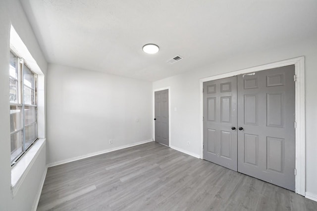 unfurnished bedroom with a closet, visible vents, baseboards, and wood finished floors