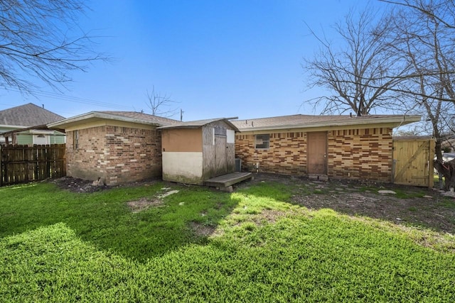 rear view of house with an outbuilding, a shed, fence, a yard, and brick siding