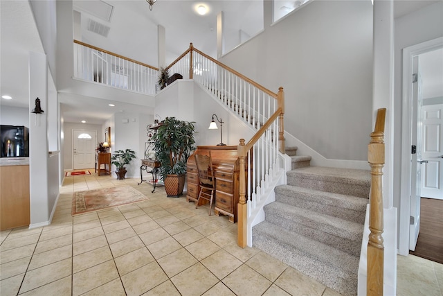 staircase featuring tile patterned floors, baseboards, visible vents, and a towering ceiling