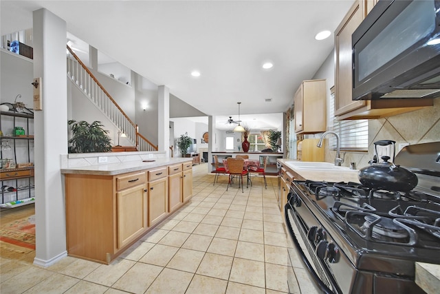 kitchen featuring light tile patterned floors, gas stove, a sink, black microwave, and backsplash