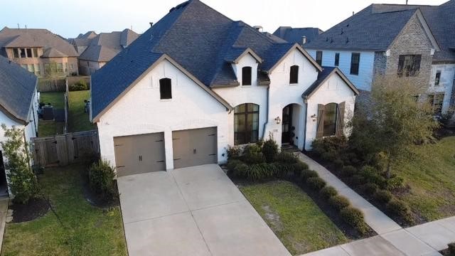 french country inspired facade featuring stucco siding, driveway, a shingled roof, and fence