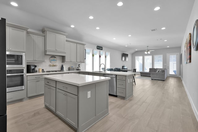 kitchen featuring a kitchen island, a peninsula, a sink, gray cabinetry, and stainless steel appliances