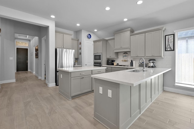 kitchen featuring tasteful backsplash, gray cabinetry, appliances with stainless steel finishes, a peninsula, and a sink