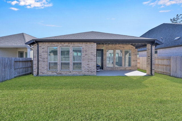 rear view of property featuring brick siding, roof with shingles, a lawn, a fenced backyard, and a patio area