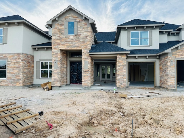 view of front of home with french doors, stone siding, roof with shingles, and an attached garage