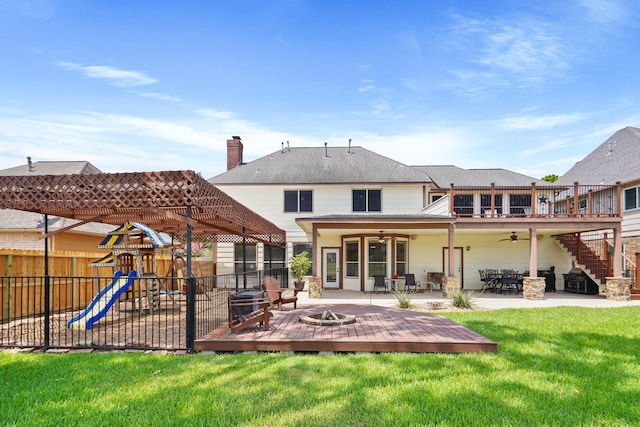 back of house featuring a fire pit, a playground, fence, a lawn, and a ceiling fan