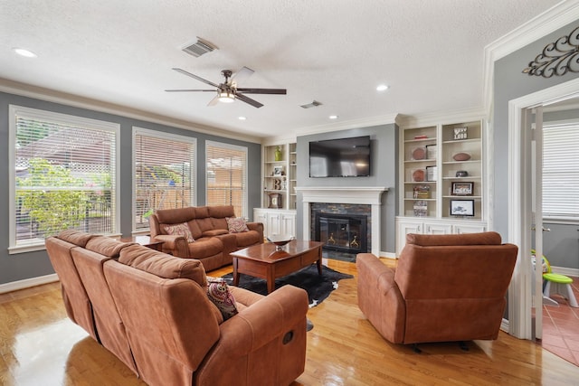 living room featuring visible vents, a fireplace with flush hearth, light wood-style floors, a textured ceiling, and crown molding