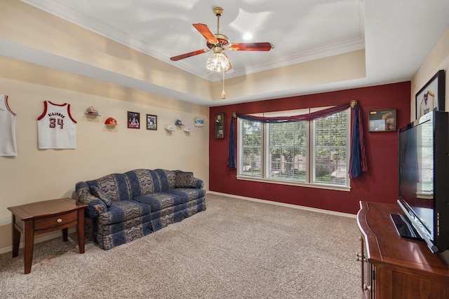 carpeted living area with ceiling fan, baseboards, a raised ceiling, and ornamental molding