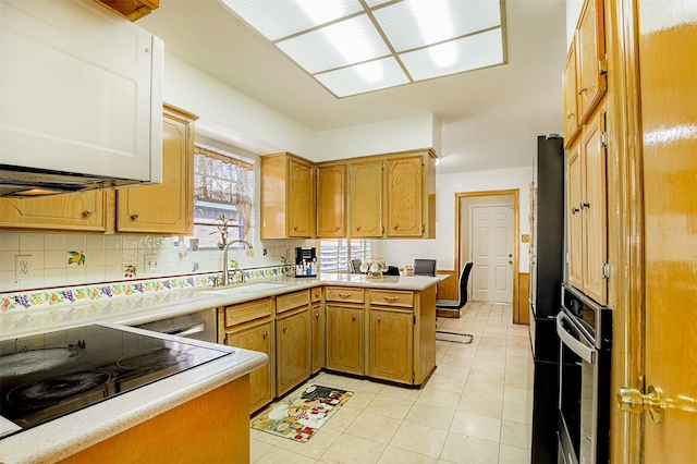 kitchen featuring oven, a sink, a peninsula, light countertops, and decorative backsplash