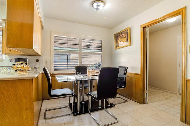 dining area with light tile patterned flooring, wainscoting, a textured ceiling, and wood walls