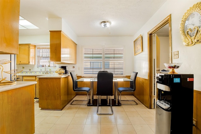 kitchen featuring a textured ceiling, a peninsula, wainscoting, light countertops, and light tile patterned floors