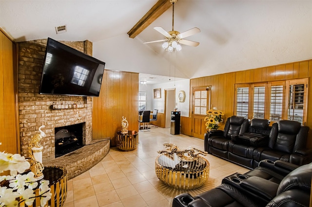 living room with visible vents, wooden walls, a brick fireplace, beamed ceiling, and light tile patterned flooring