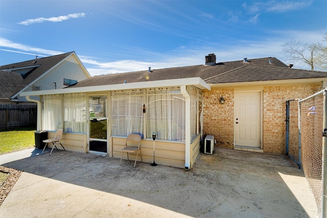 rear view of house featuring a patio, fence, roof with shingles, brick siding, and a chimney