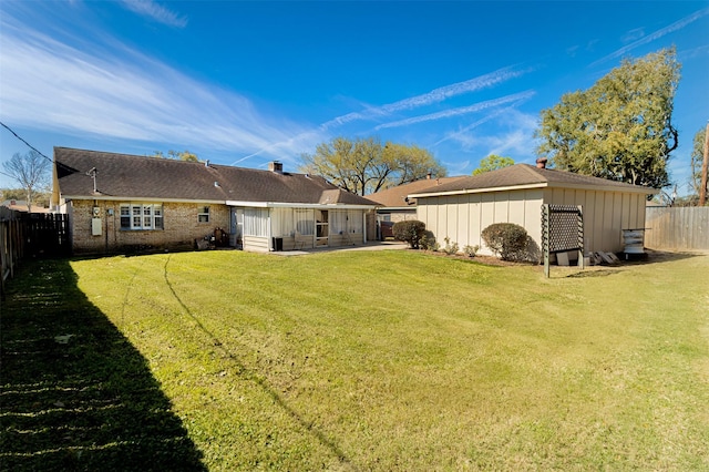 rear view of house with board and batten siding, a yard, a fenced backyard, a patio area, and an outbuilding