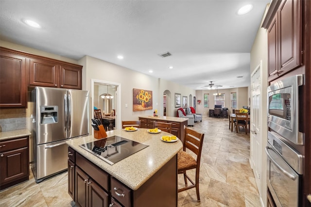 kitchen featuring a kitchen island, open floor plan, stone tile floors, appliances with stainless steel finishes, and arched walkways