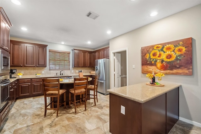 kitchen featuring visible vents, a sink, backsplash, appliances with stainless steel finishes, and a breakfast bar area