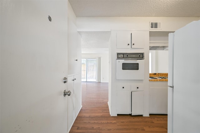 kitchen featuring white appliances, dark wood-style floors, visible vents, white cabinets, and a textured ceiling